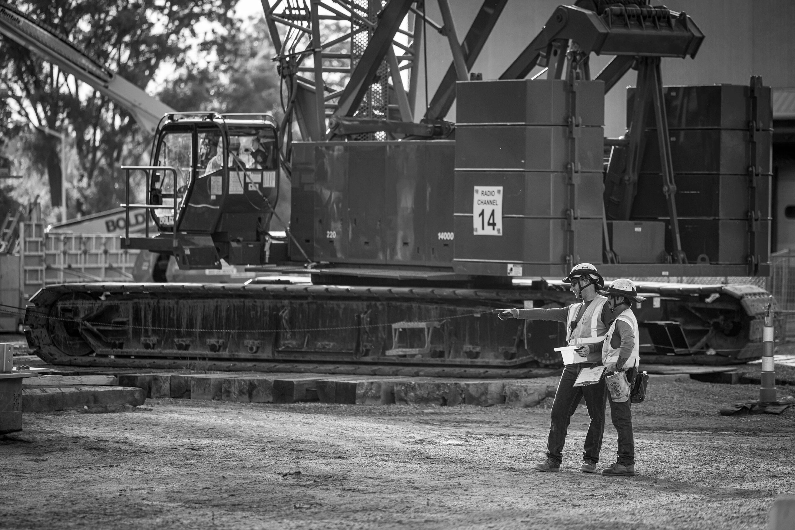 Two construction project managers reviewing plans in front of a large crane